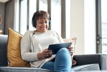 Woman wearing headphones while relaxing on a couch using a tablet